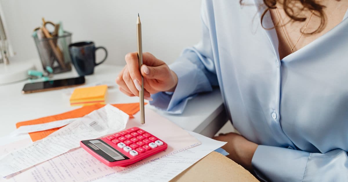 A woman holding a pencil and working through bills with a calculator and papers at her desk