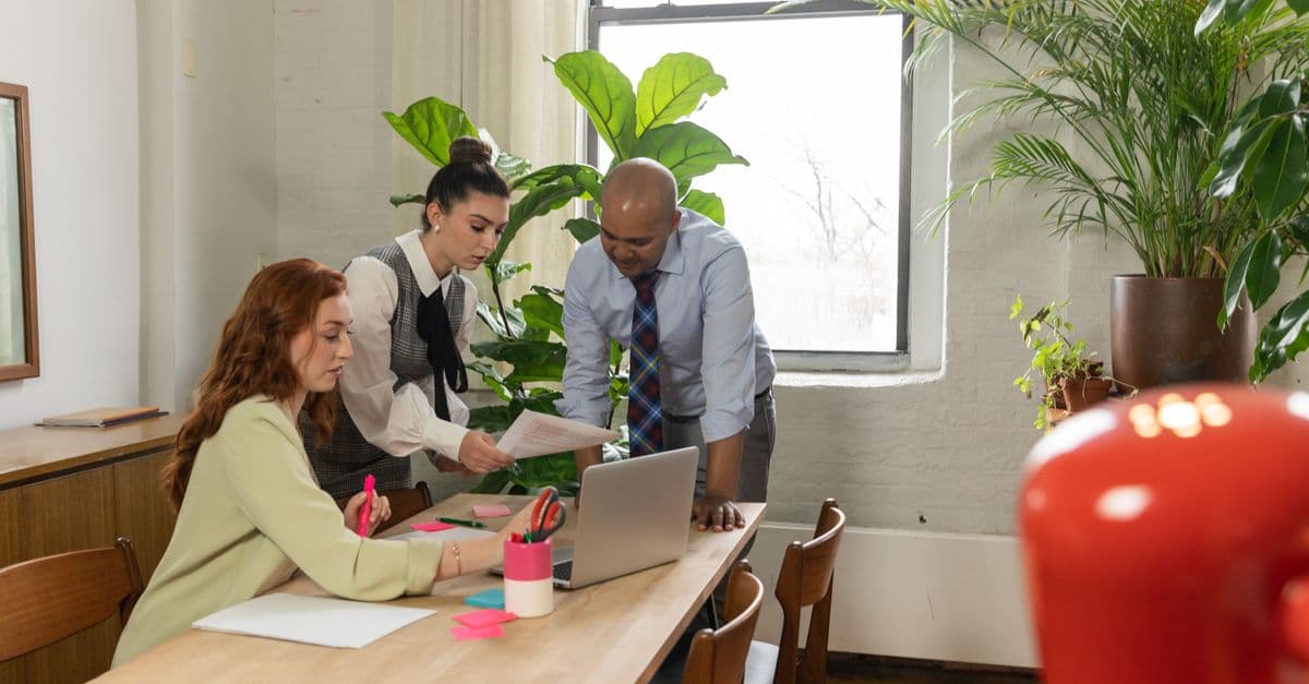 Three colleagues talk through a plan at a shared table in a bright office.