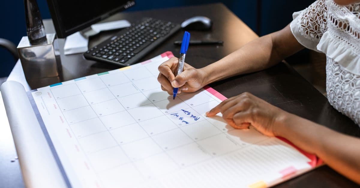 A person writing in a paper desk calendar with a pen